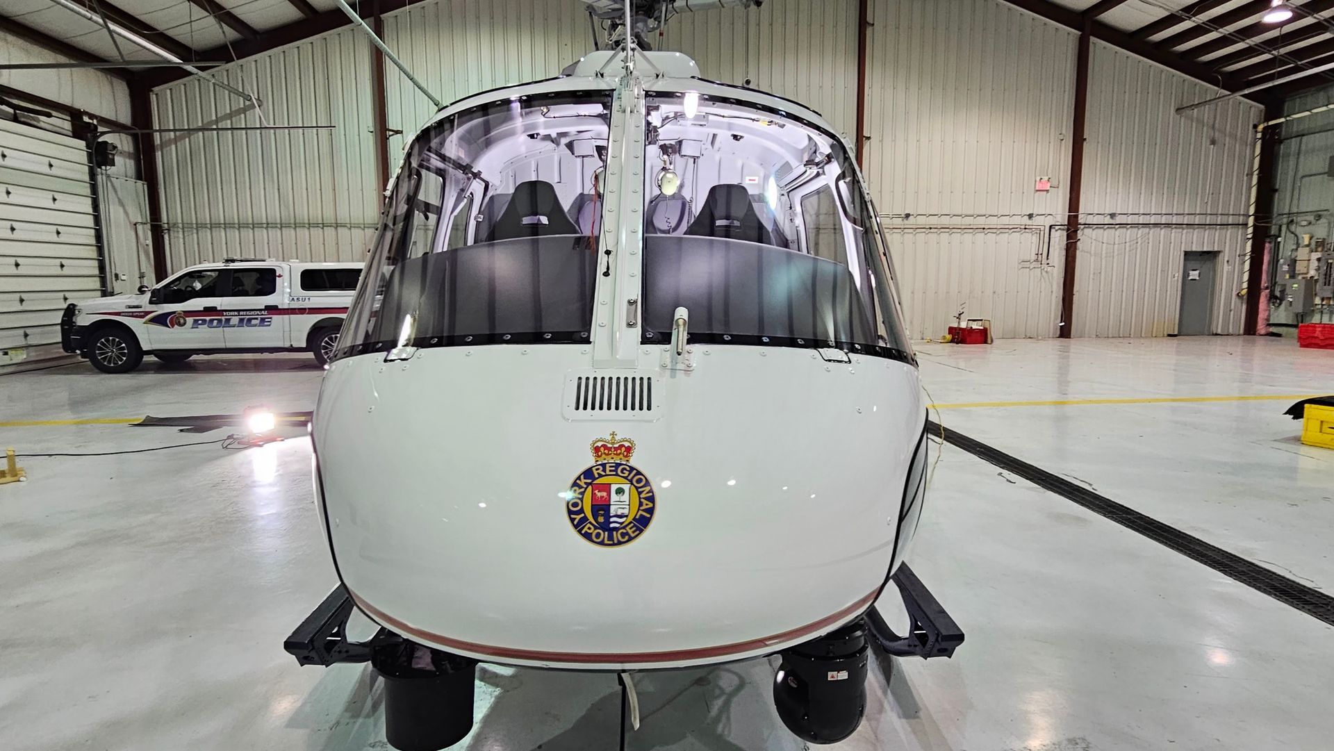 White helicopter in a hangar with a police car in the background. Royal crest on the nose.