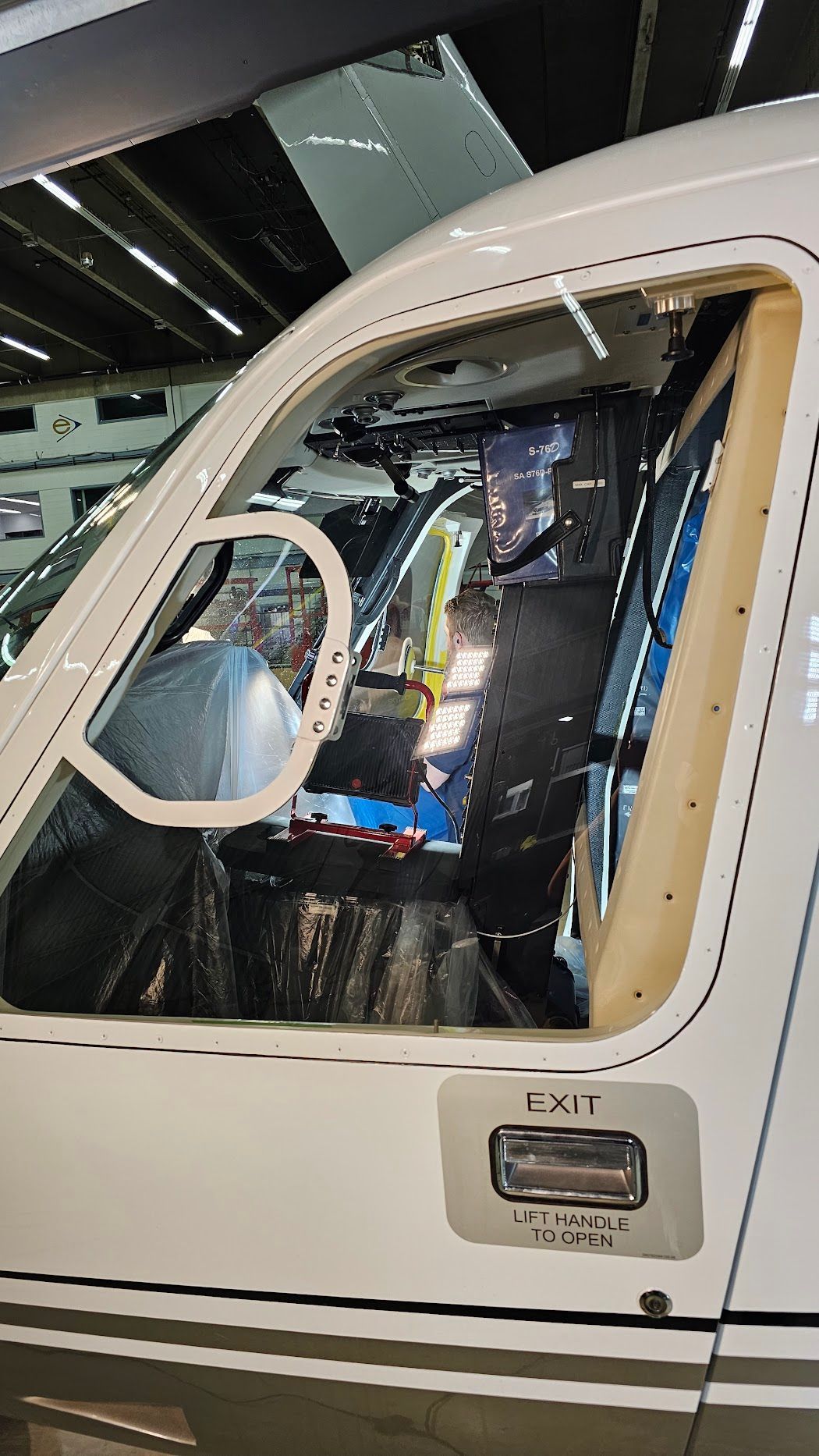 Cockpit of a helicopter with open window frames, revealing interior components and workshop setting.