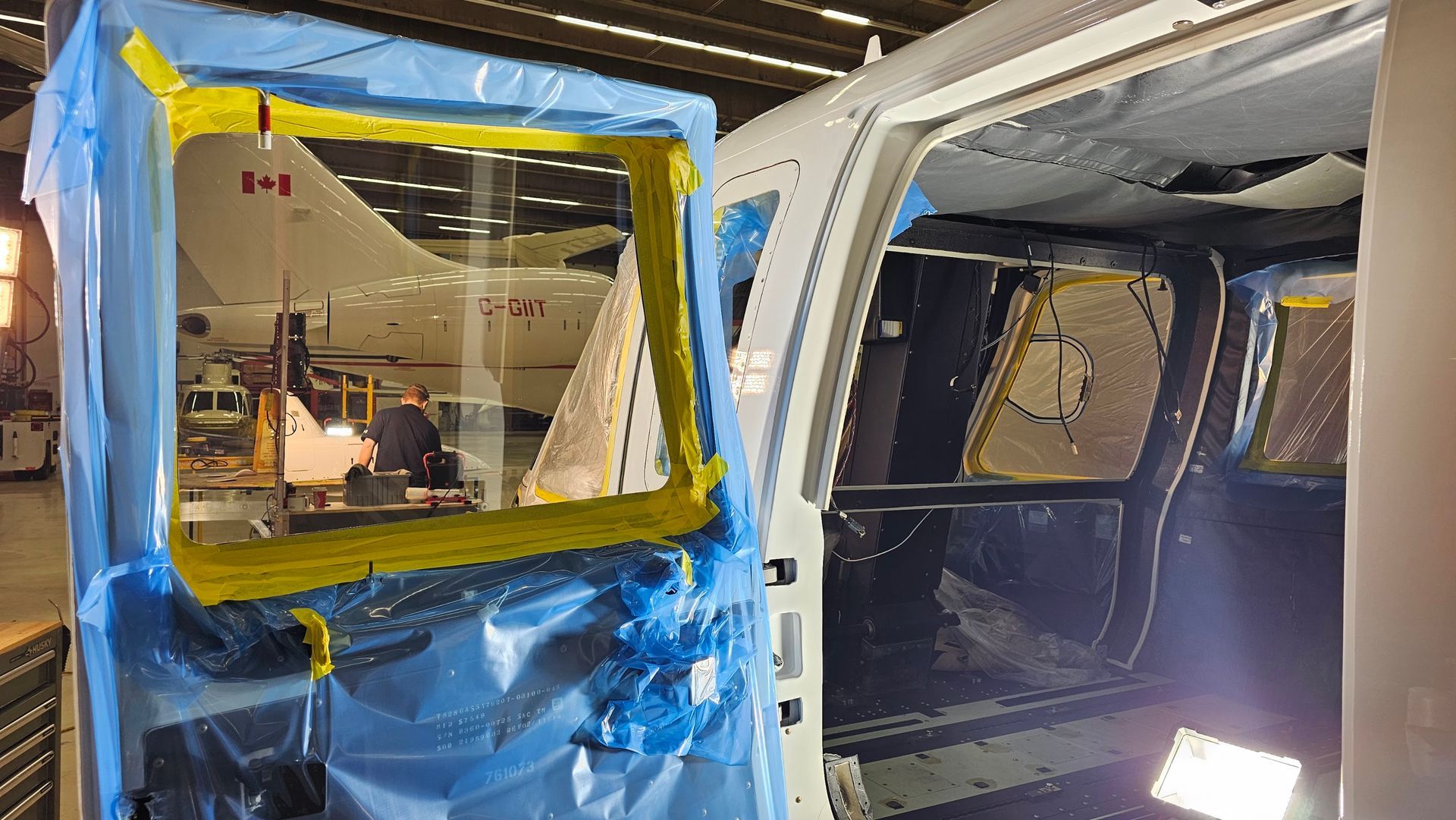 Aircraft door taped with blue and yellow material, interior partially visible in a hangar.