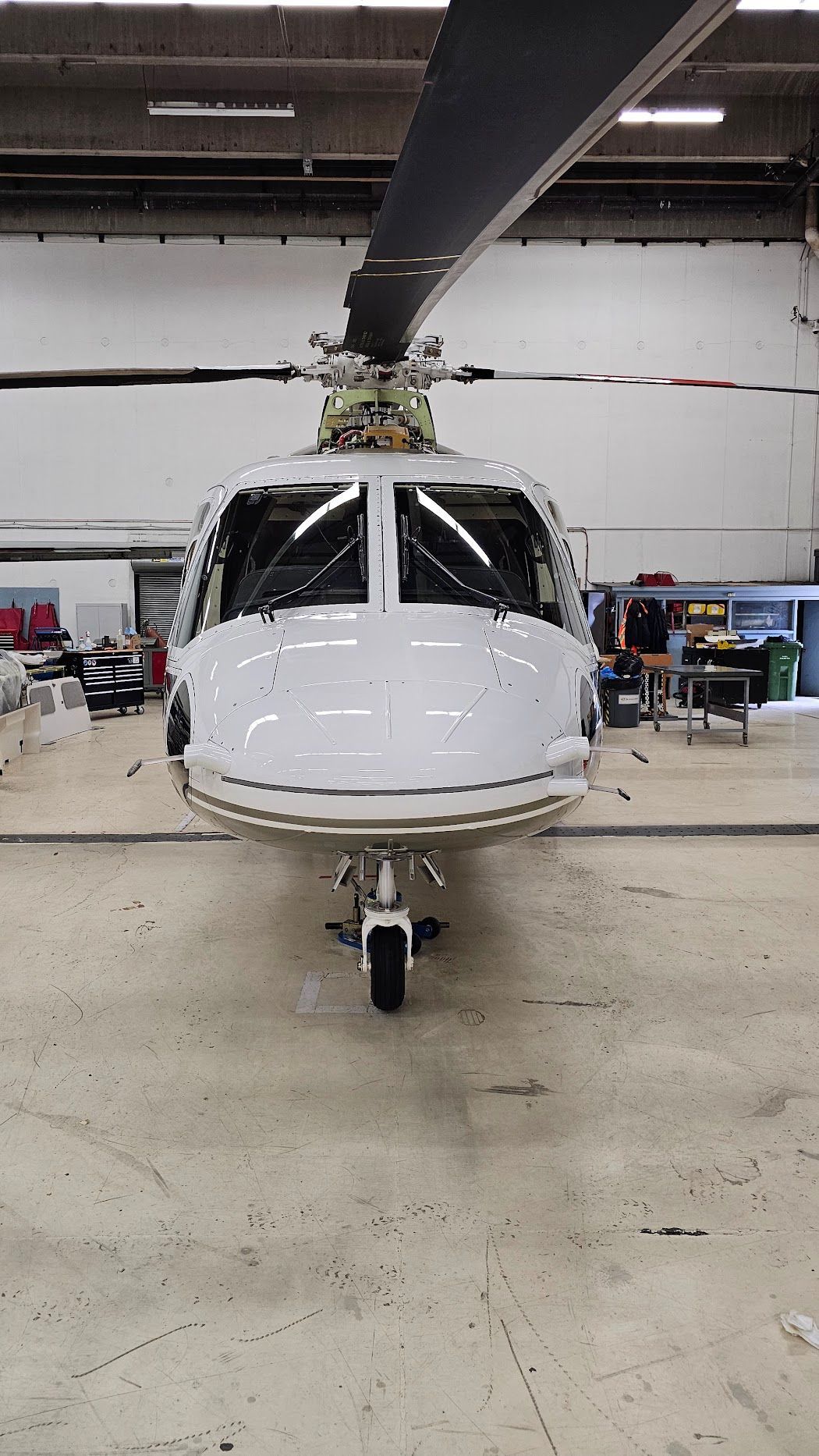 White helicopter in a hangar, facing forward. Tail rotor blades visible.