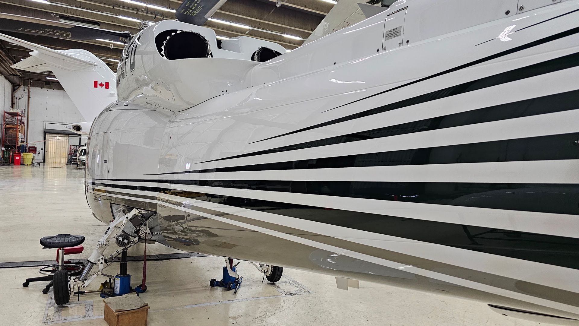 White and black striped airplane in a hangar, Canadian flag visible.