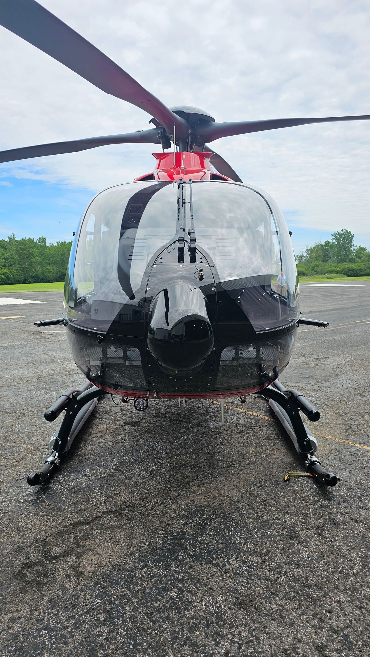 Black helicopter on the ground, front view, red accents, clear cockpit, cloudy sky background.