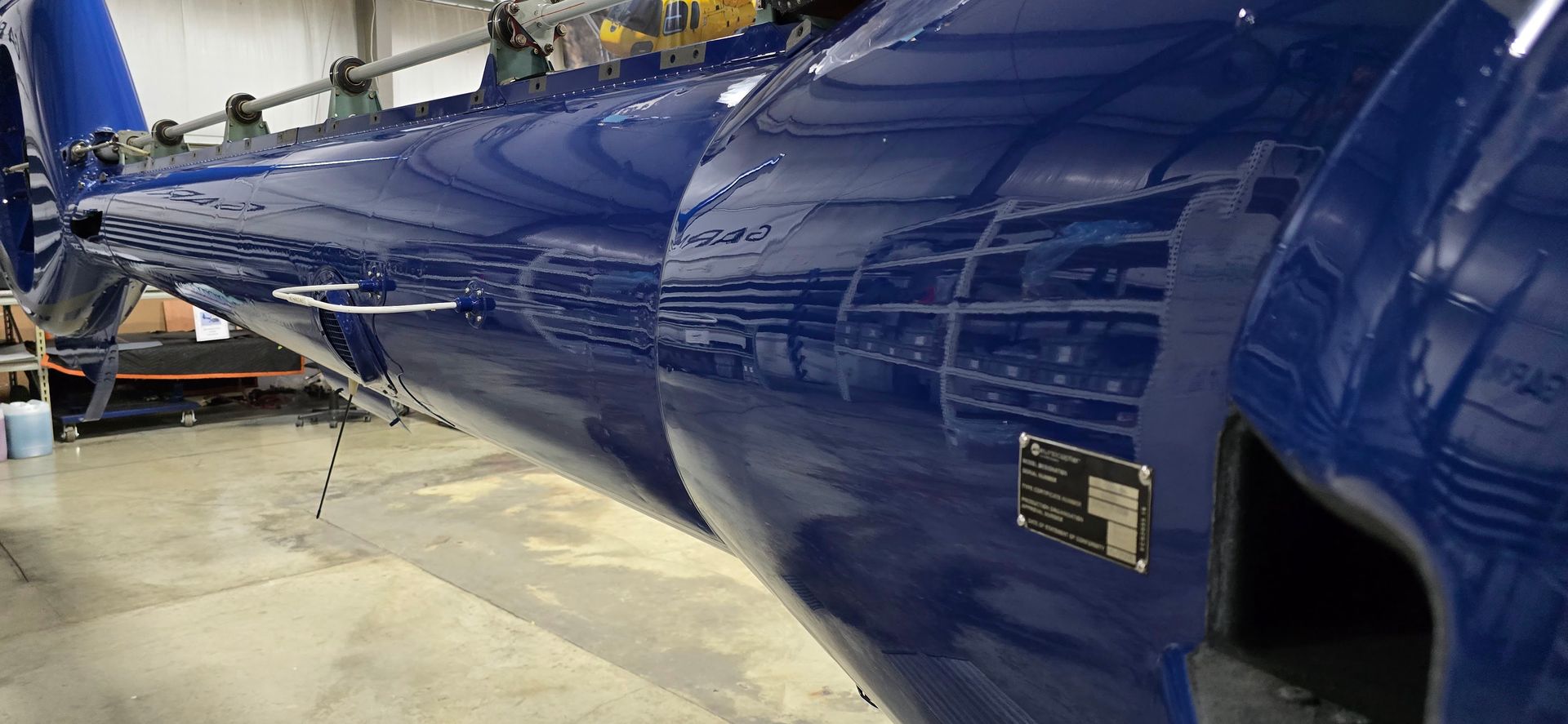 Blue helicopter fuselage in a workshop, reflecting the surroundings.