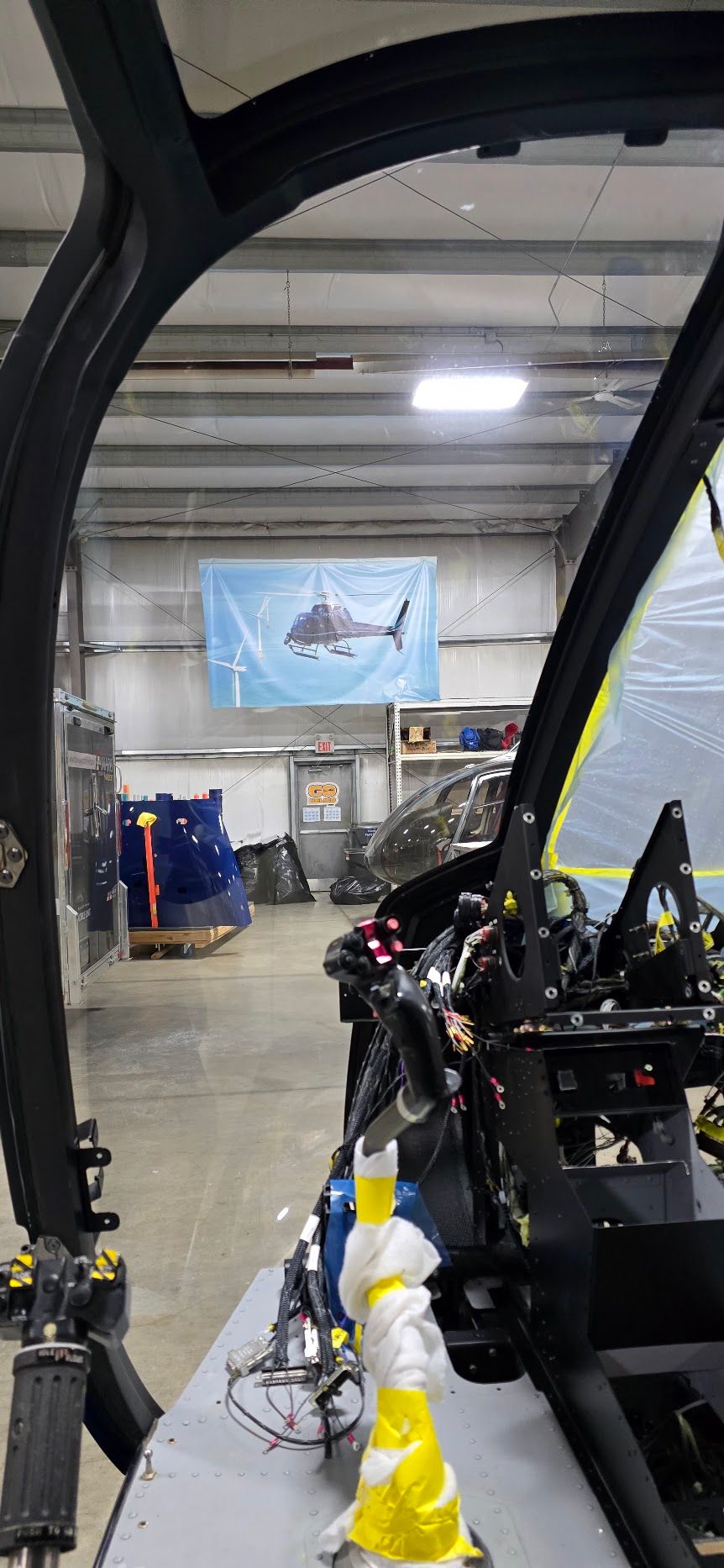 View from inside a helicopter cockpit looking at a flag with a shark symbol in a factory.