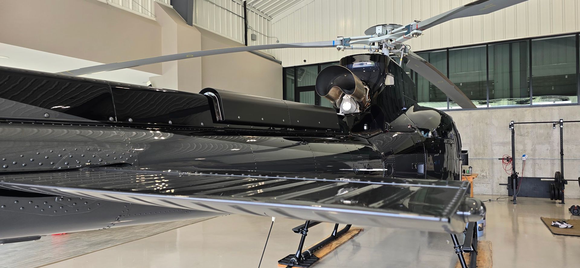 A black helicopter with rotor blades inside a hangar.