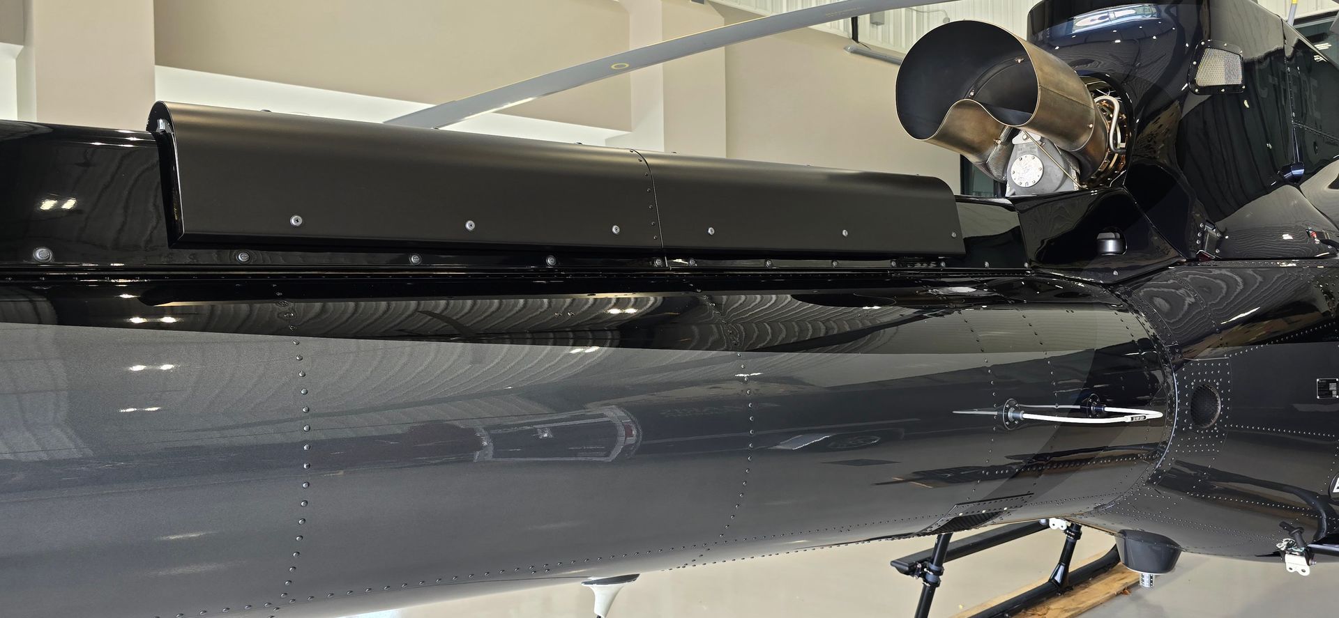 Person working on a black vehicle with a roof-mounted black panel. White ceiling and a light reflect off the glossy surface.