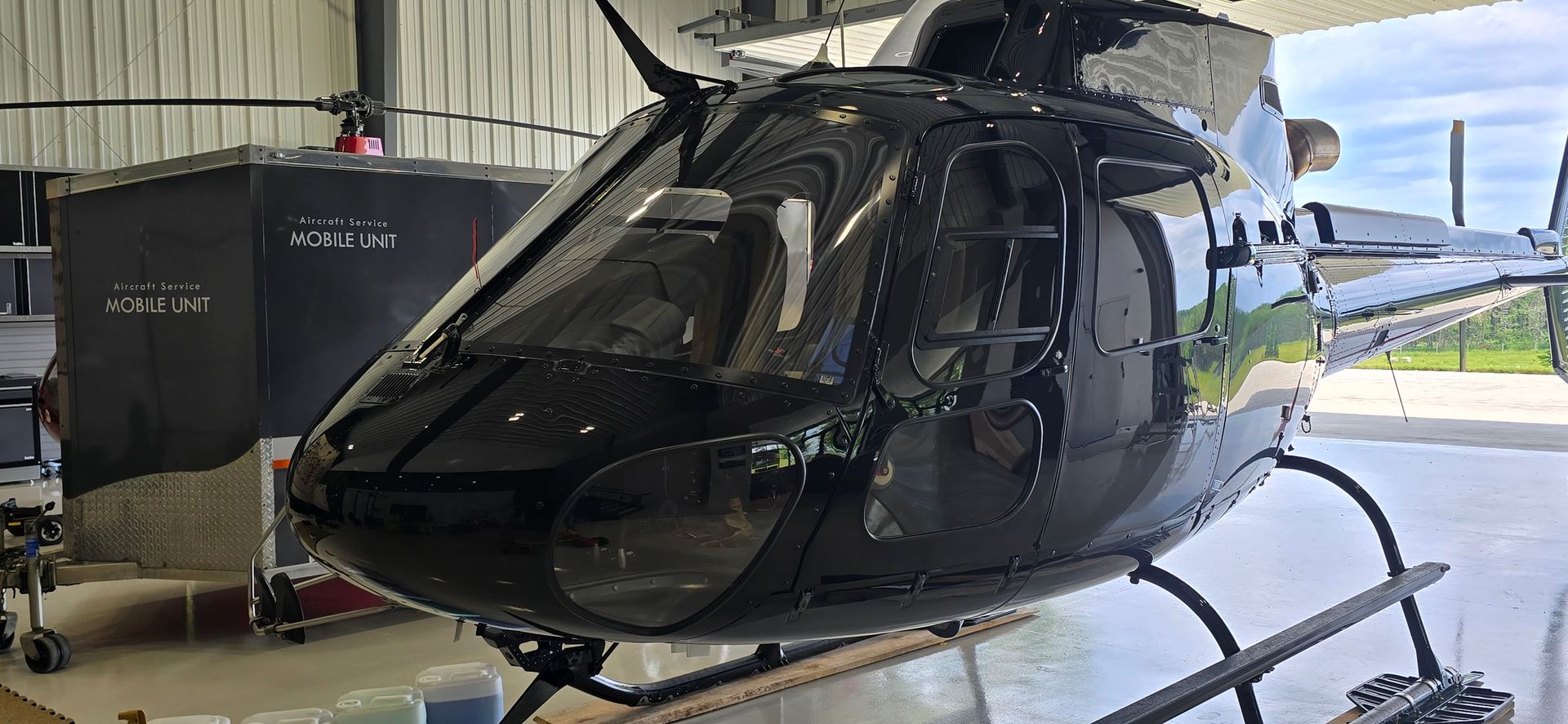 Black helicopter parked inside a hangar, sunlight reflecting off the glossy surface.