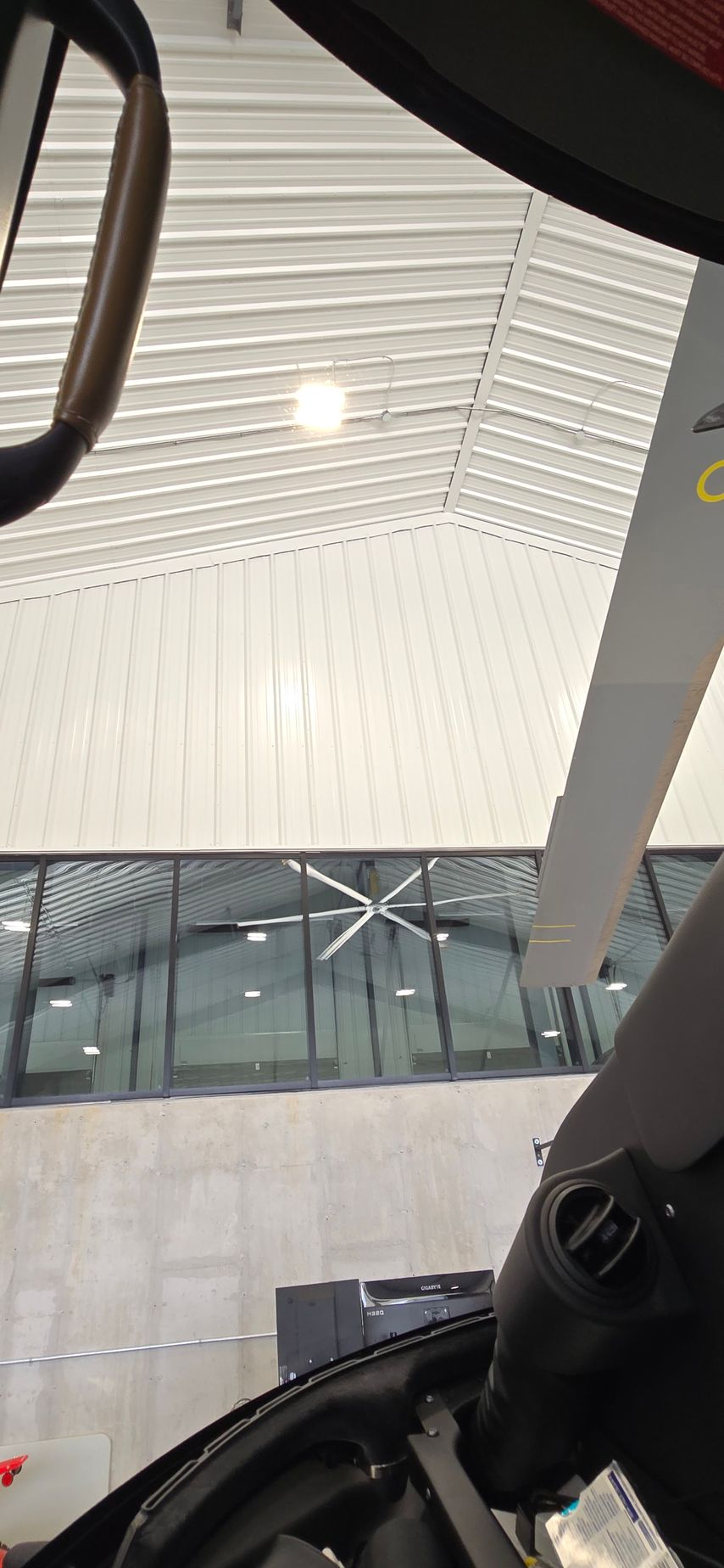 View of a building's from inside a vehicle. The ceiling has parallel white panels and a large windowed wall is visible.
