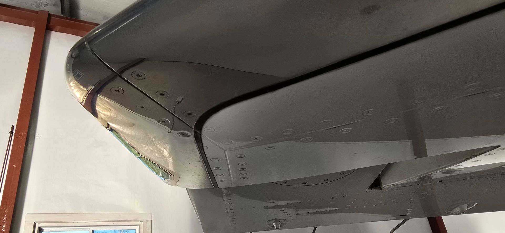 Underside of a plane's wing showing its curved edge, rivets, and underside of aileron.