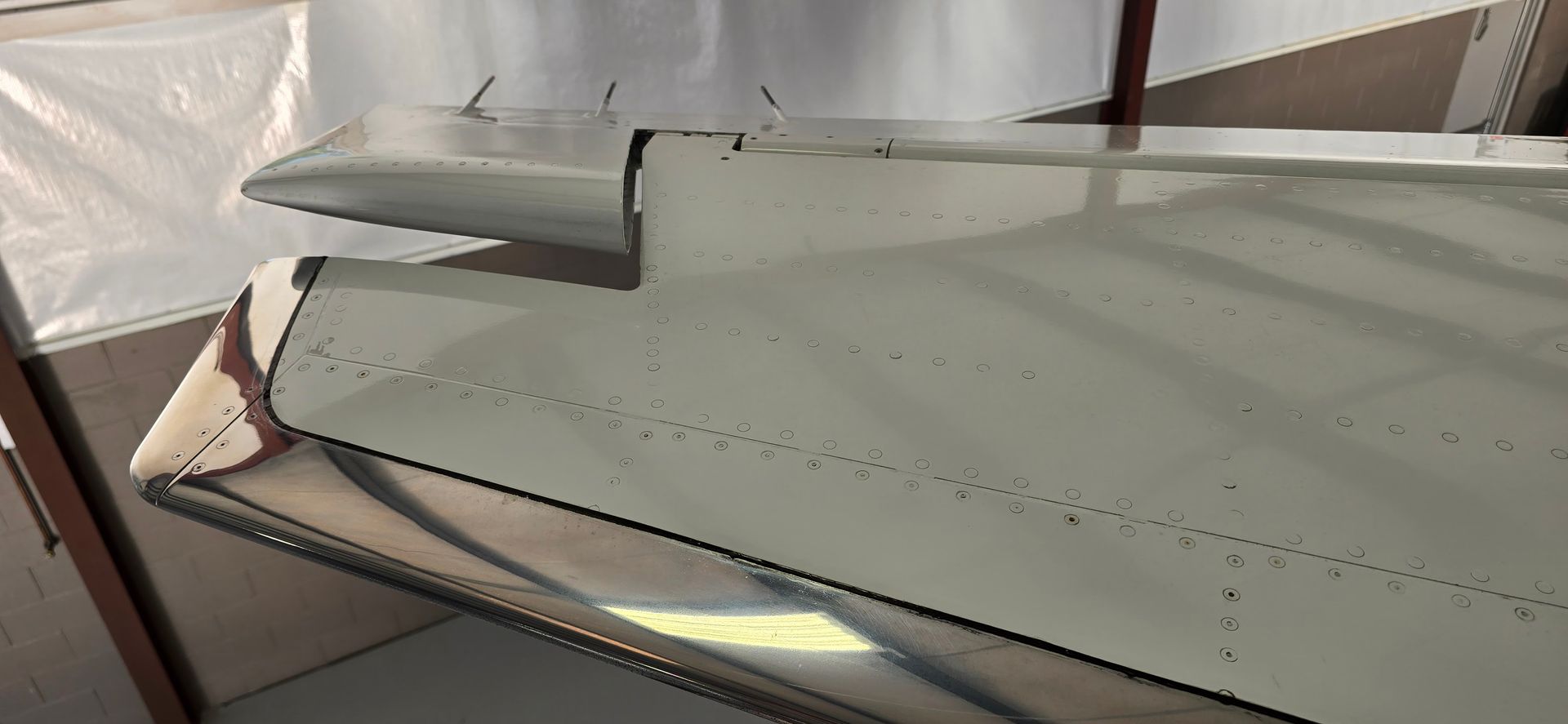 White aircraft wing with rivets. The wing is partially exposed, showing the underside and a smaller section on top.