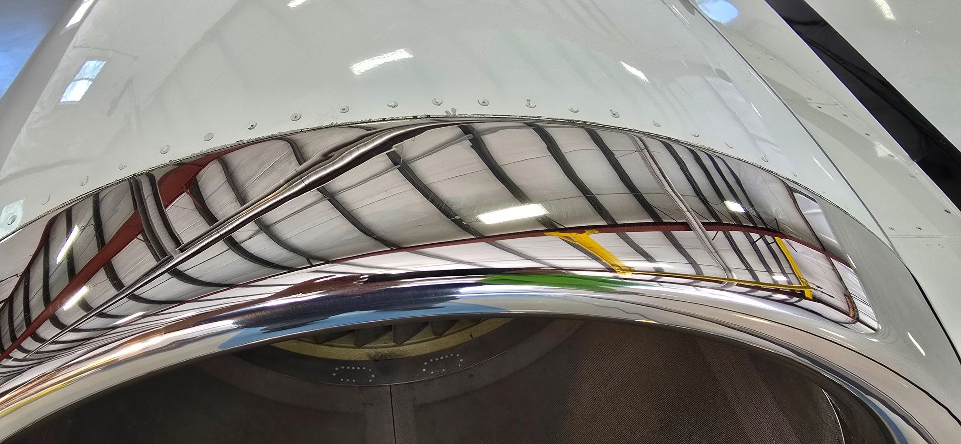 Close-up of a shiny, curved aircraft component reflecting a warehouse interior.