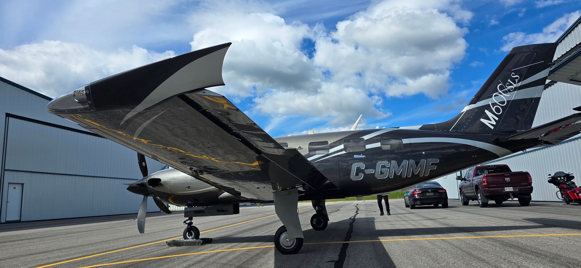 A black and silver airplane with raised wings on a tarmac in front of a blue sky and white clouds.