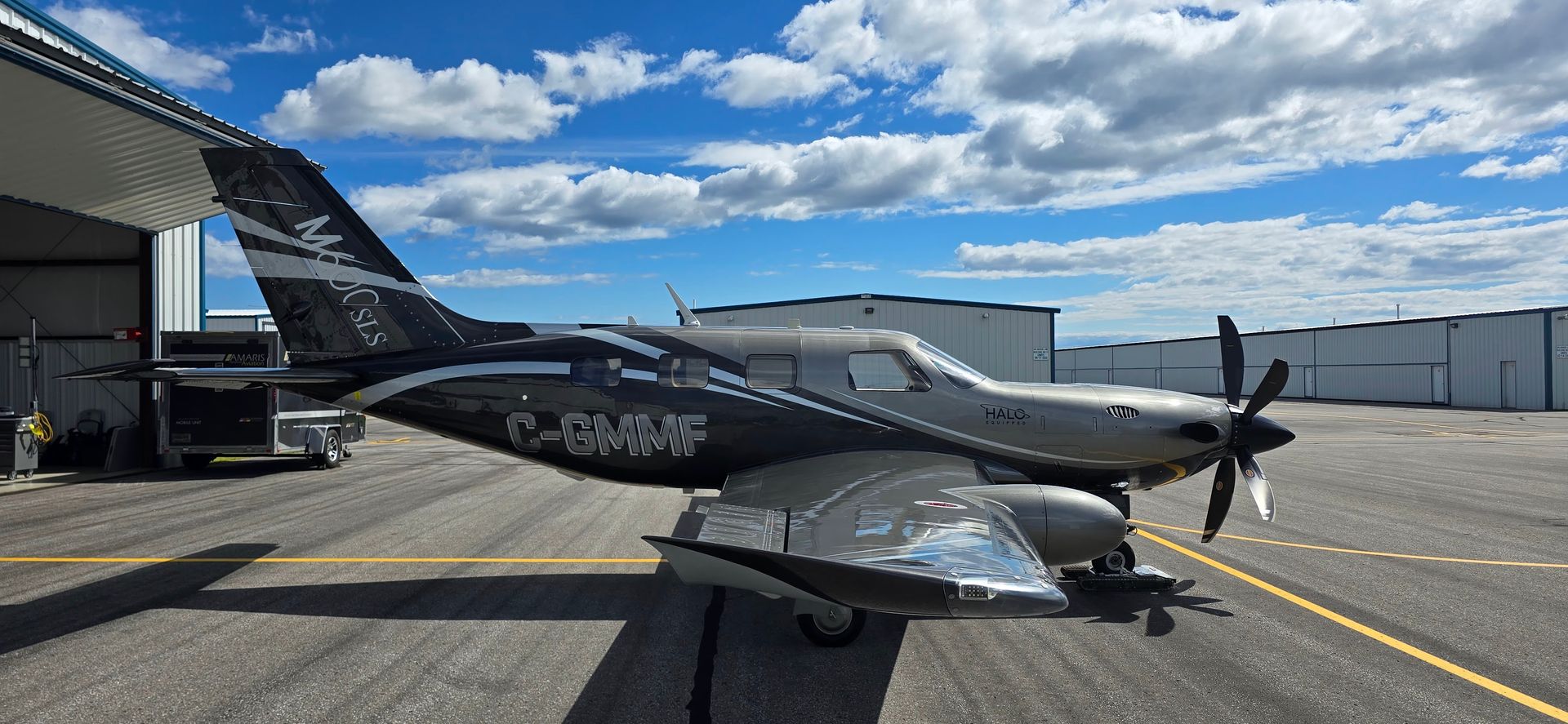 Two airplanes on an airfield under a blue, cloudy sky. One plane is black, the other silver.