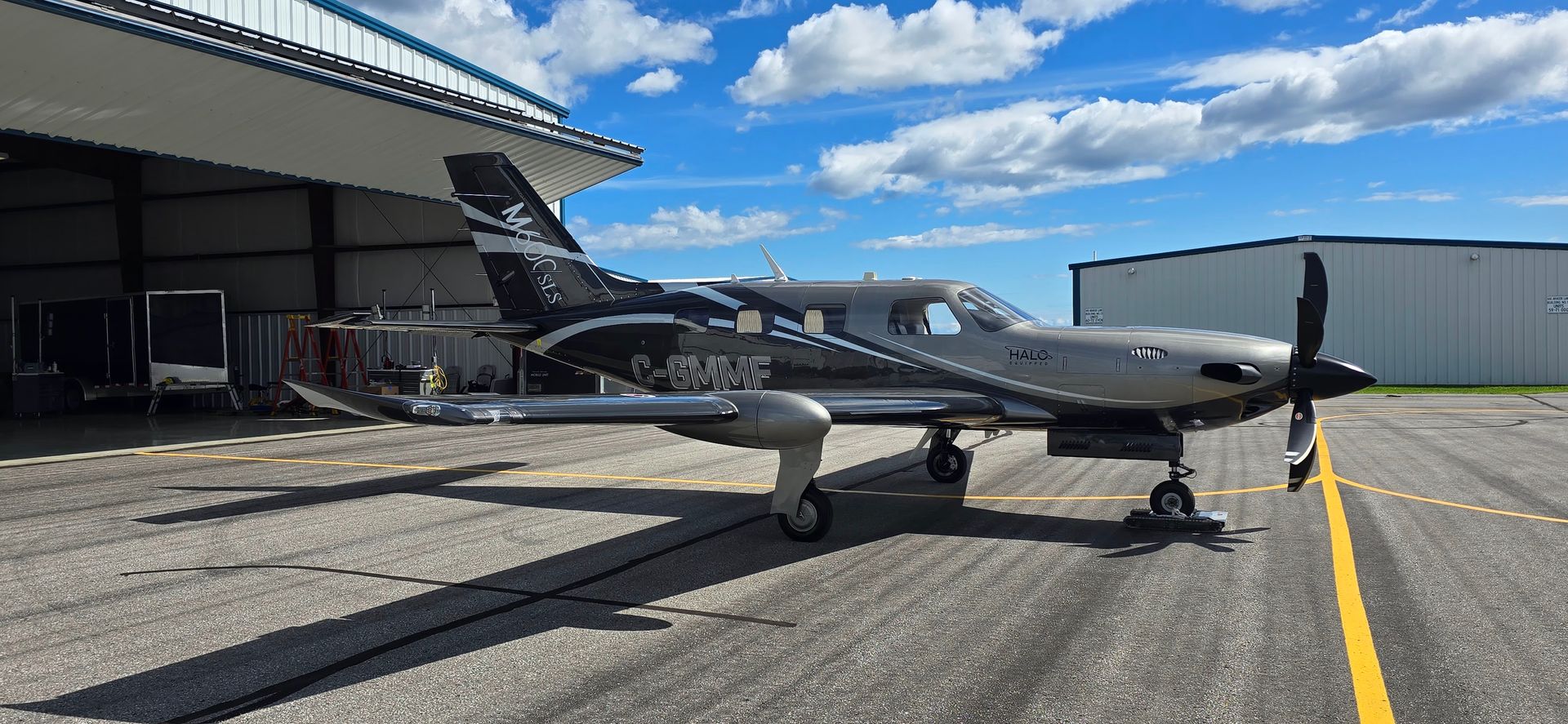 A small airplane on a runway next to a hangar under a blue sky with clouds.