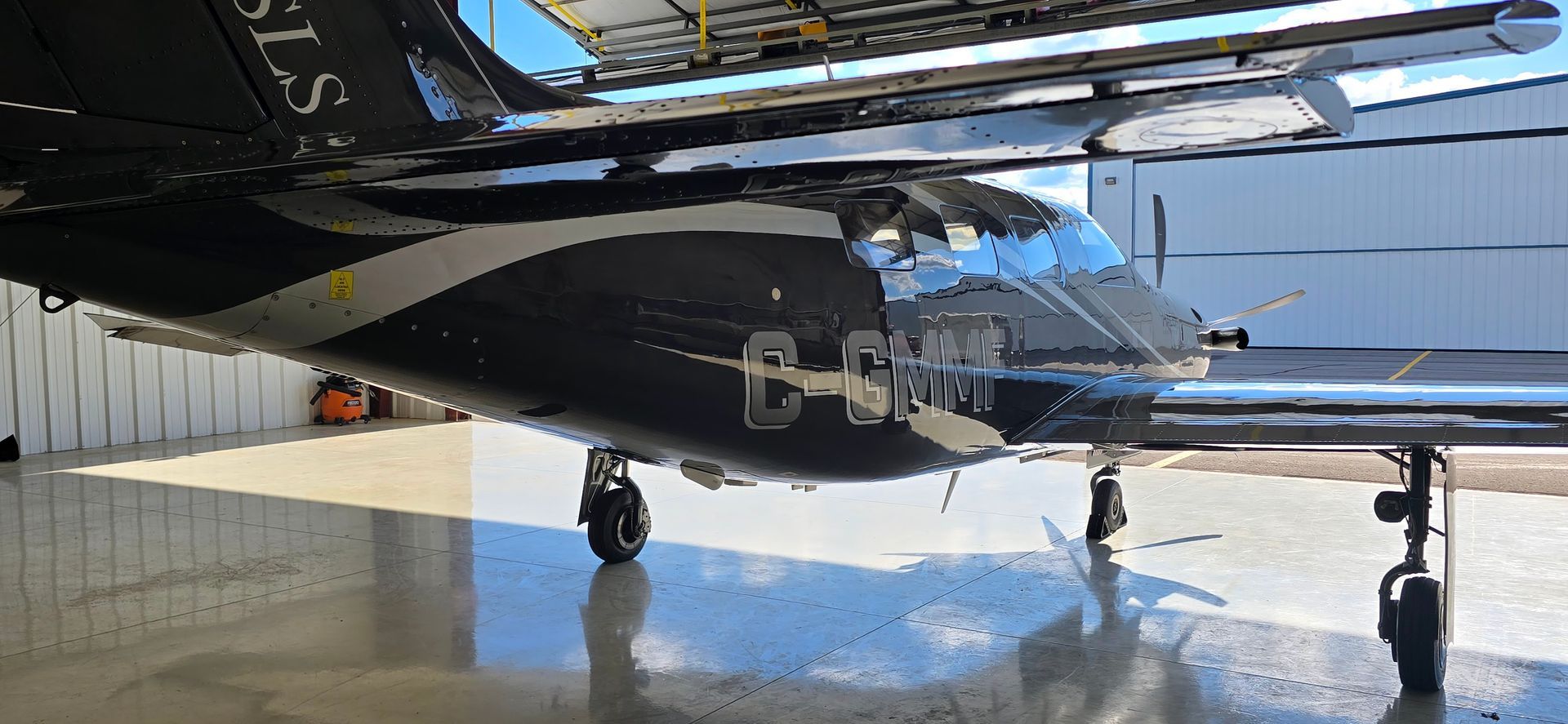 Black airplane with white accents in a hangar, registration C-FMRJ.