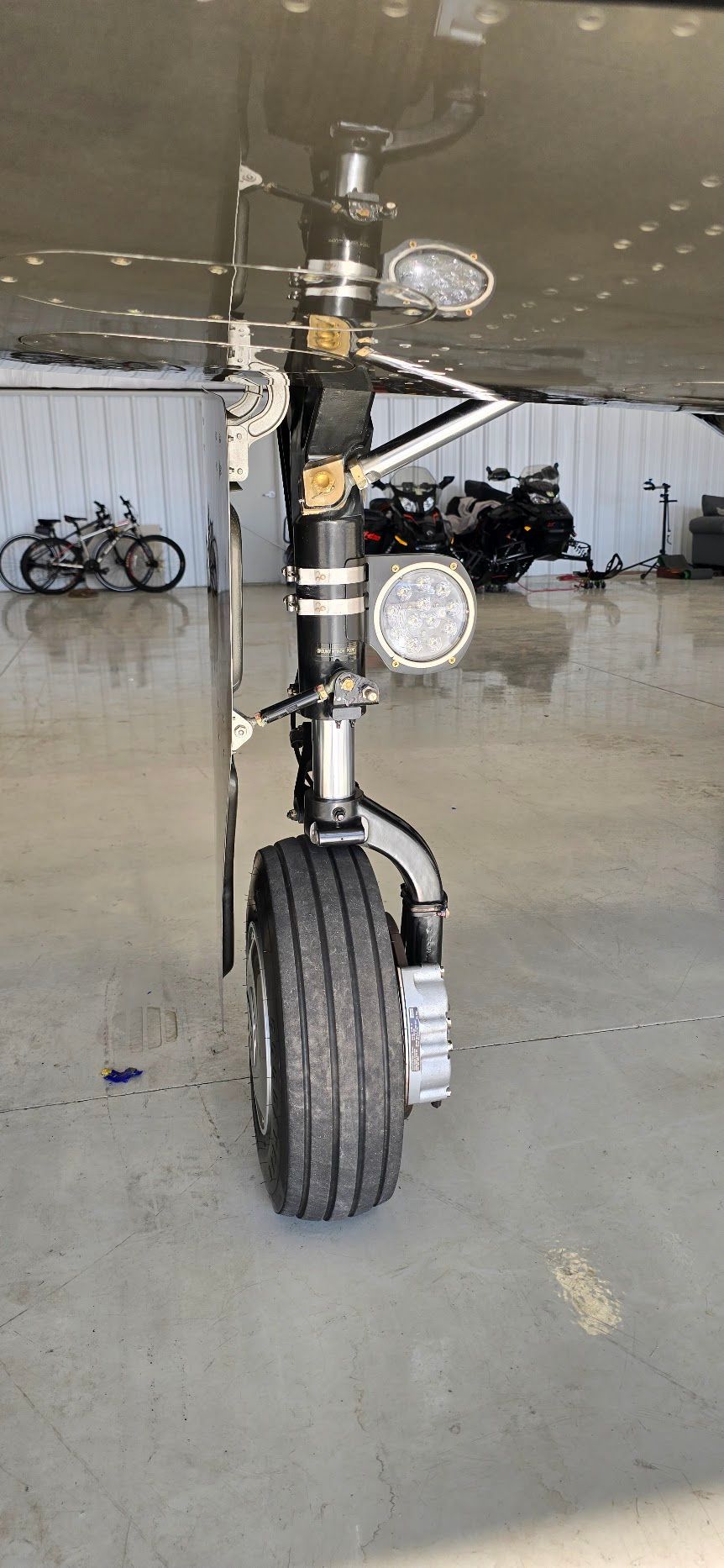 Aircraft landing gear with tire and lights, viewed from the ground in a hangar.