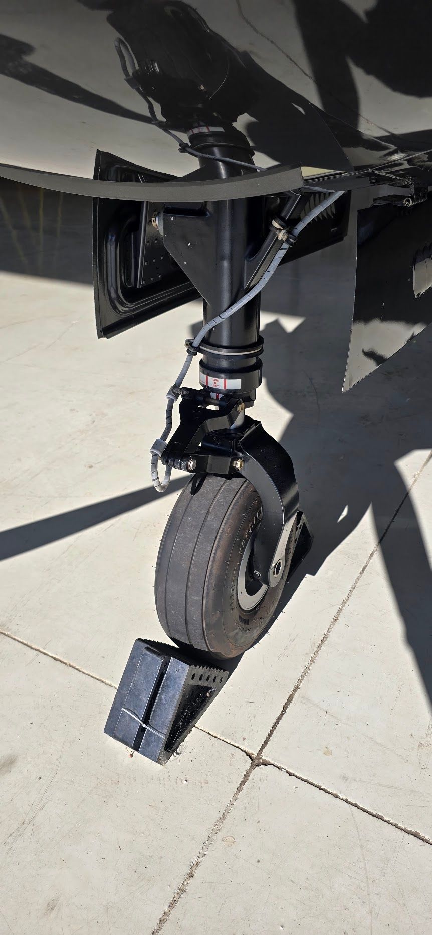 Aircraft tire on the ground with a wheel chock. Black landing gear and tire on a concrete surface.