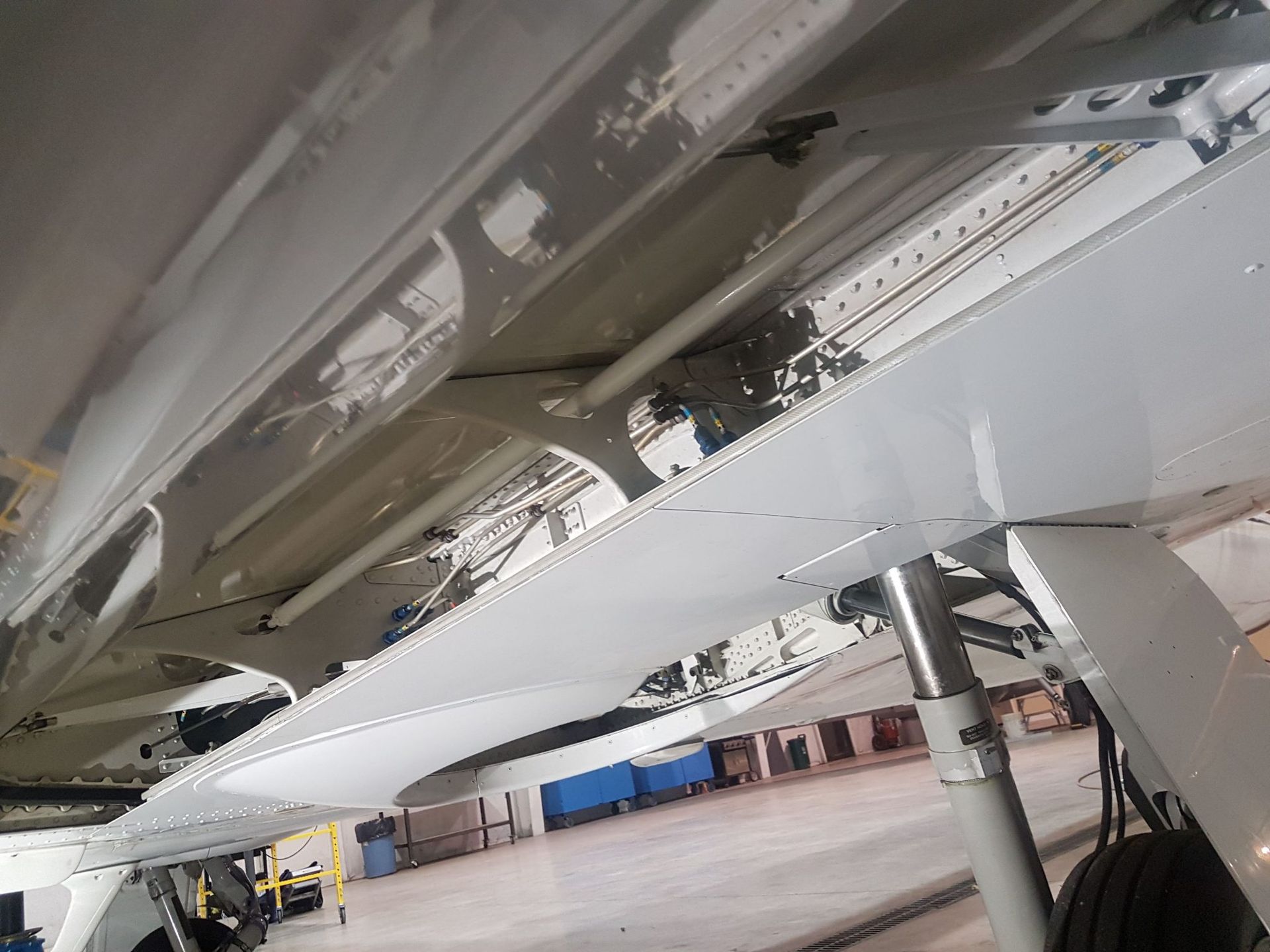 Underside of a white aircraft wing. Rivets, struts, and landing gear visible against a light grey background.