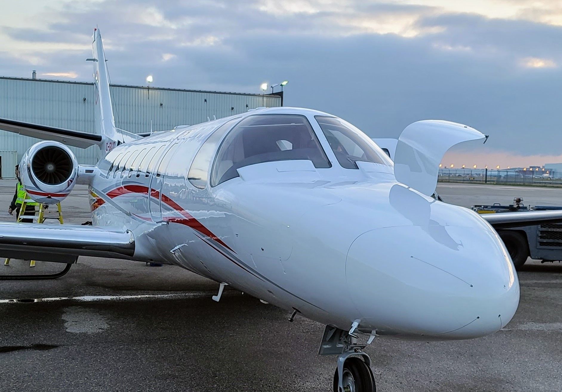 White private jet on a tarmac with red accents, cockpit open.