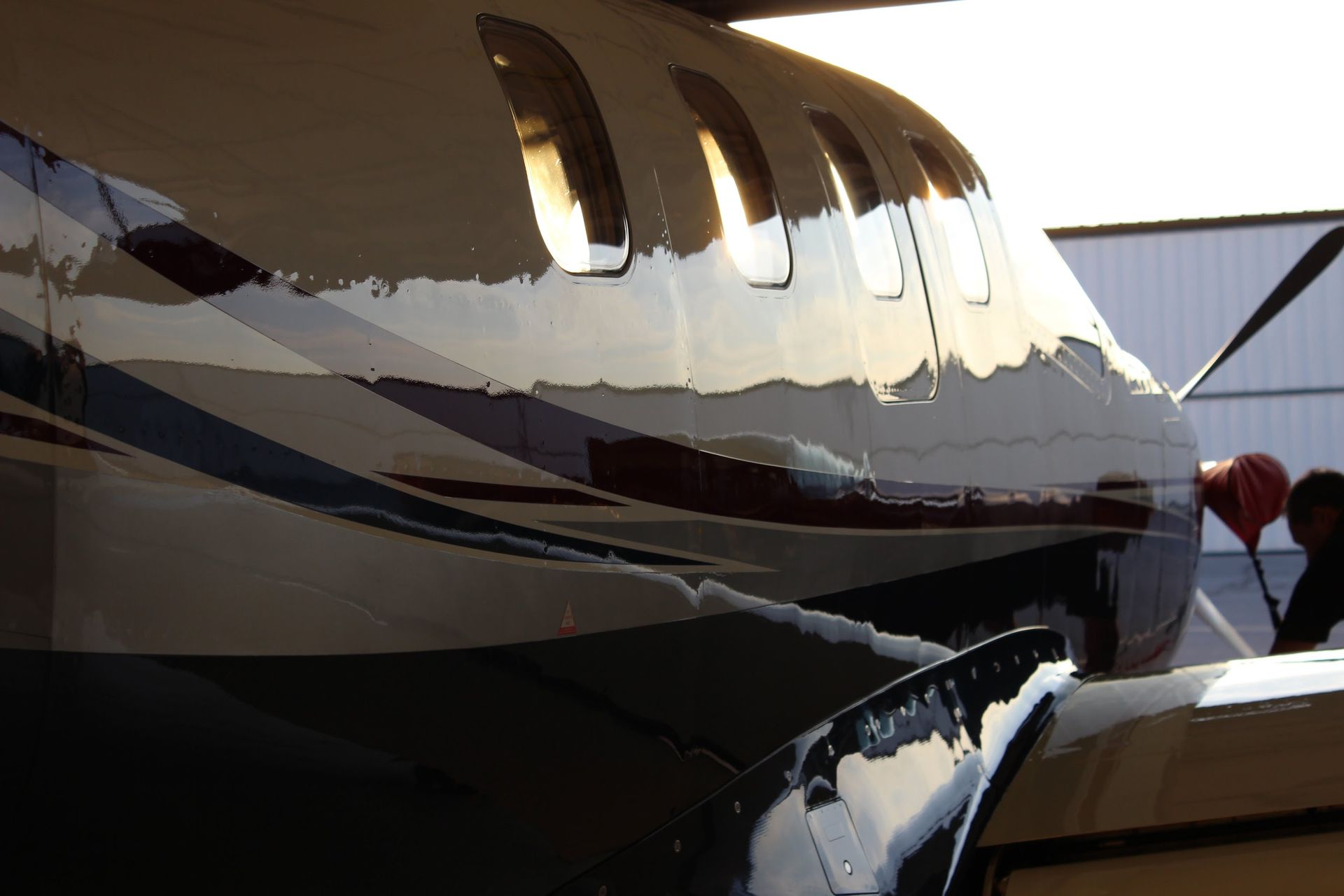 Airplane fuselage with reflective paint, dark blue, white, and red stripes, with oval windows.