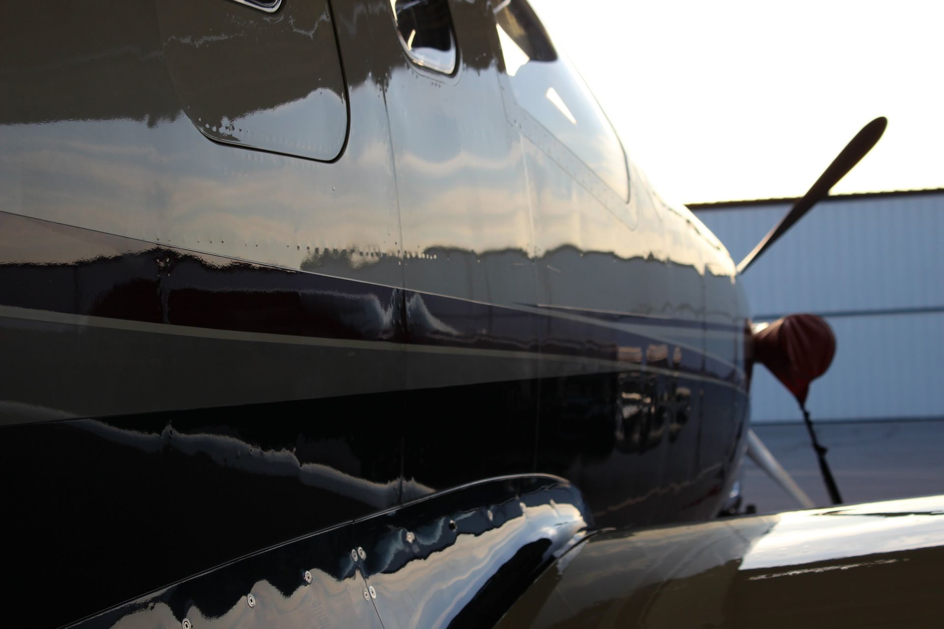 Close-up of a shiny airplane exterior with a propeller. The fuselage reflects the sky and buildings.