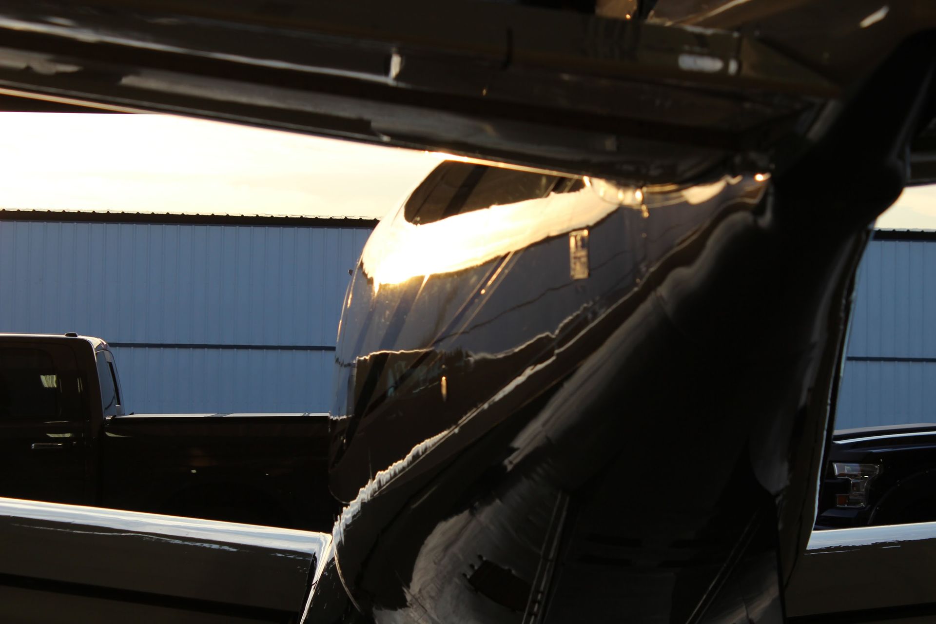 Tail of a black airplane with the sun reflecting off its shiny surface.
