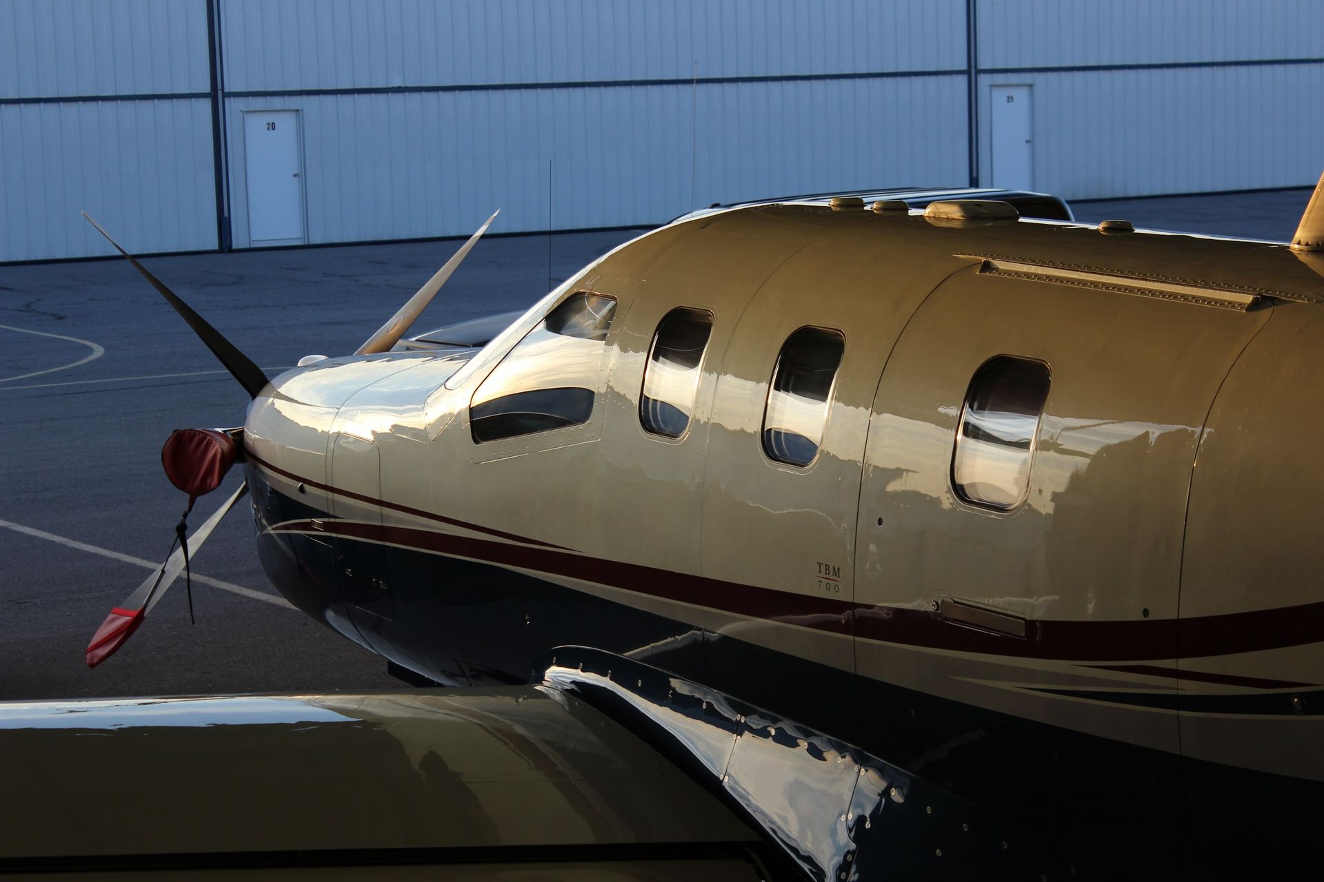Turboprop airplane parked on tarmac in front of a hangar. Propeller and windows visible.