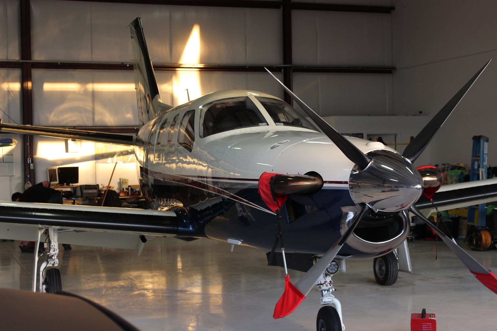 Airplane with blue and white body and silver propeller in a hangar.