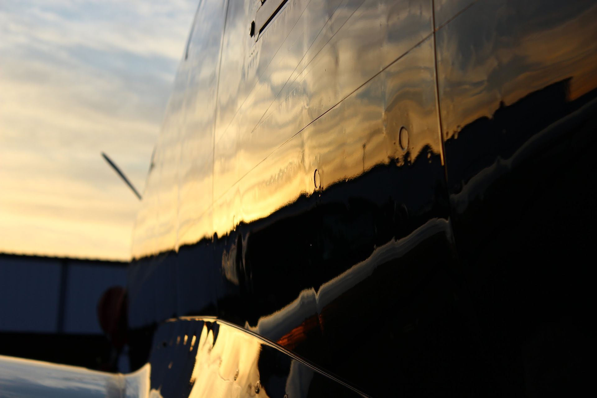 Reflective surface of a dark blue plane reflects a sunset, creating golden and orange hues.