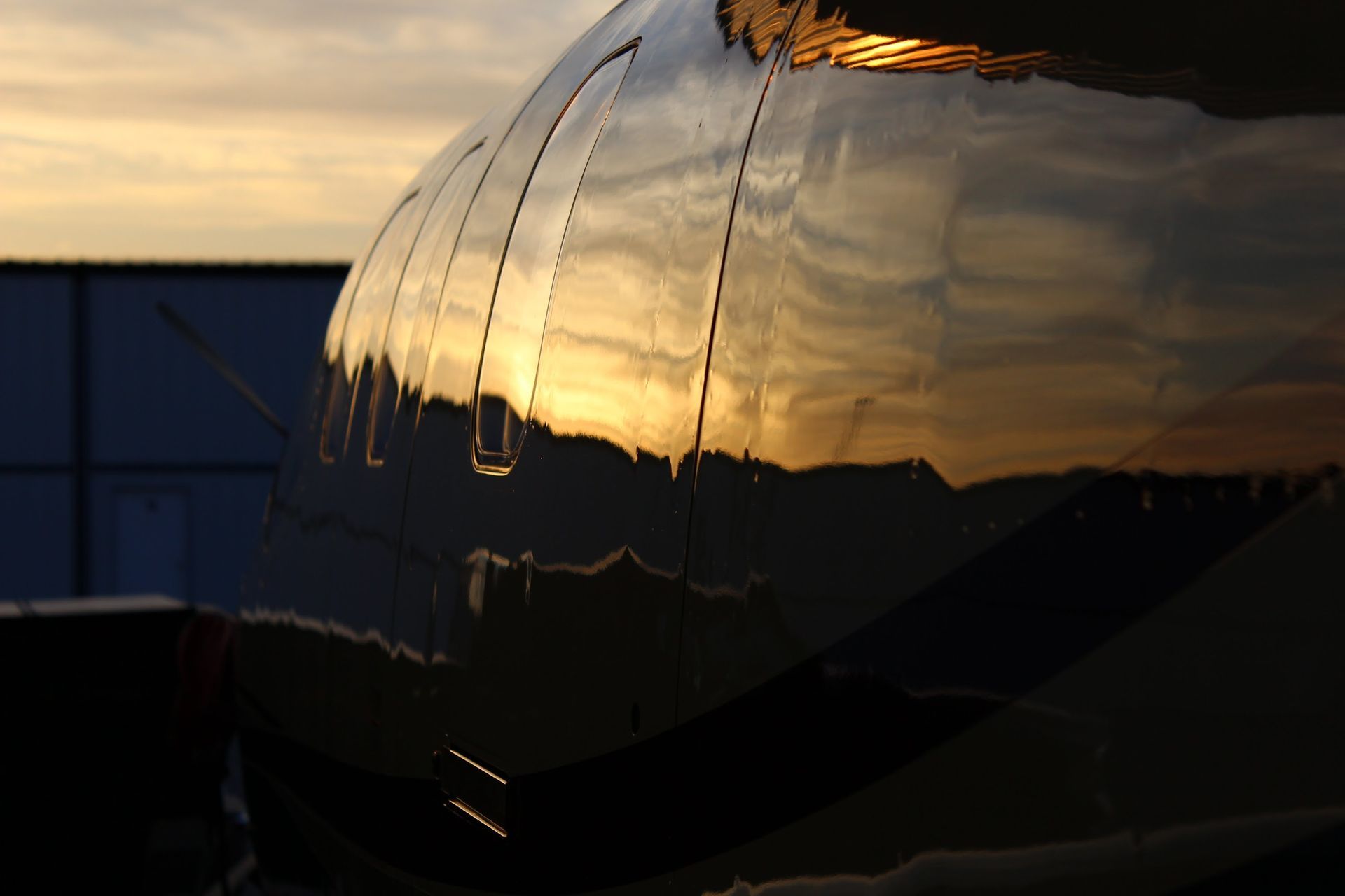 Shiny airplane fuselage reflects a sunset with orange and gold hues.