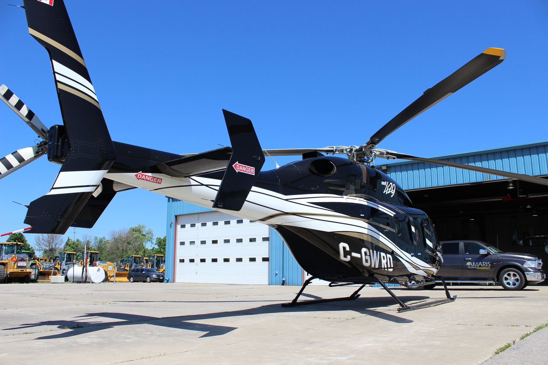 Black and white helicopter on a tarmac, parked in front of a hangar; blue sky.