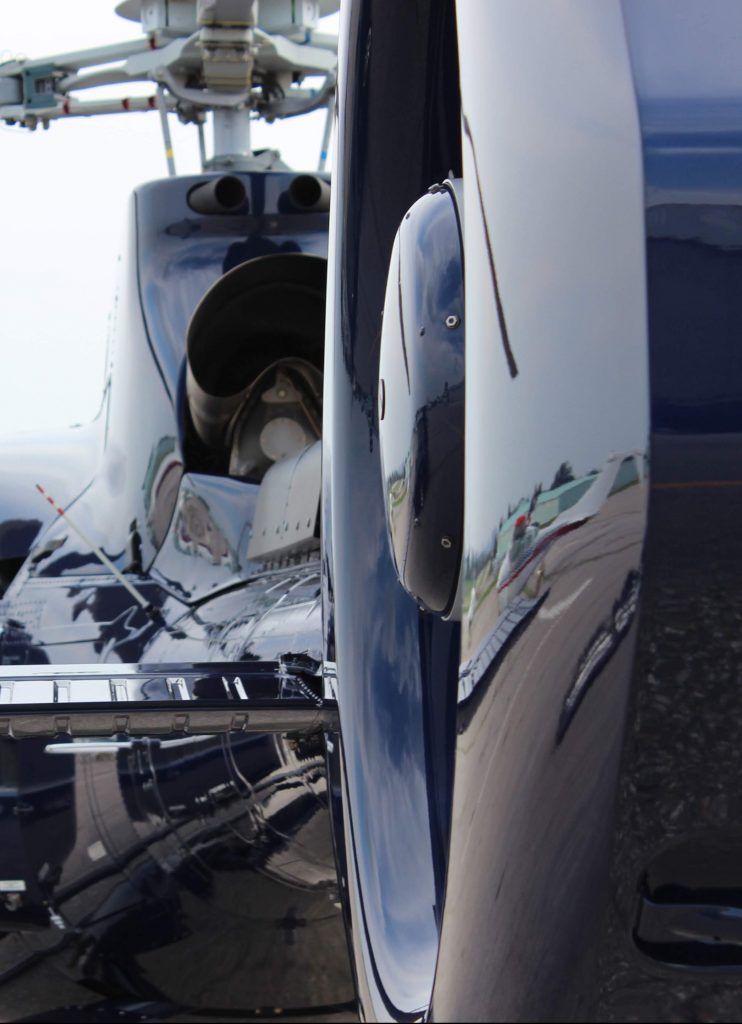 Tail of a black helicopter with reflective surfaces, reflecting a runway and sky.