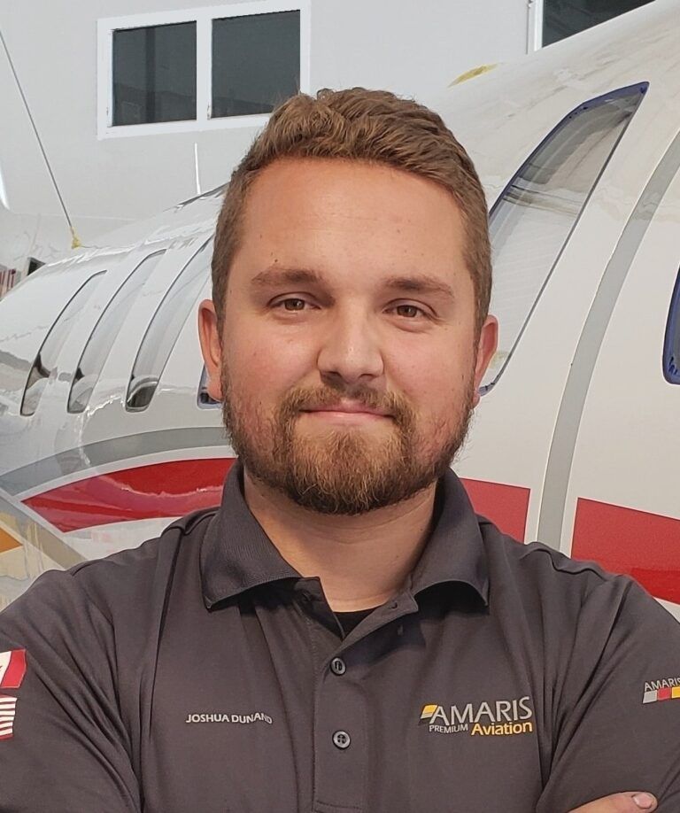 Man with a beard in a gray polo shirt stands in front of an airplane. The shirt has a logo.