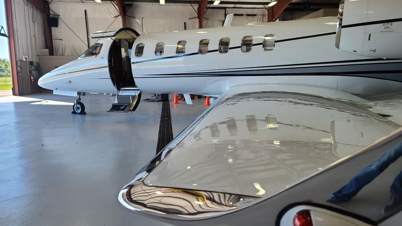 White private jet with open door in a hangar, showing a reflective wing and silver trim.