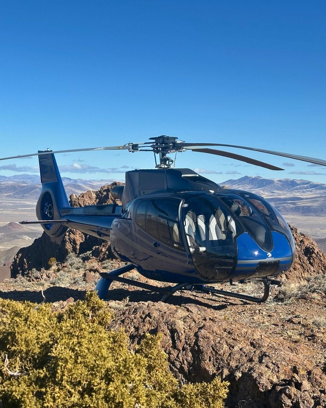 Blue helicopter on a rocky mountaintop against a clear blue sky.