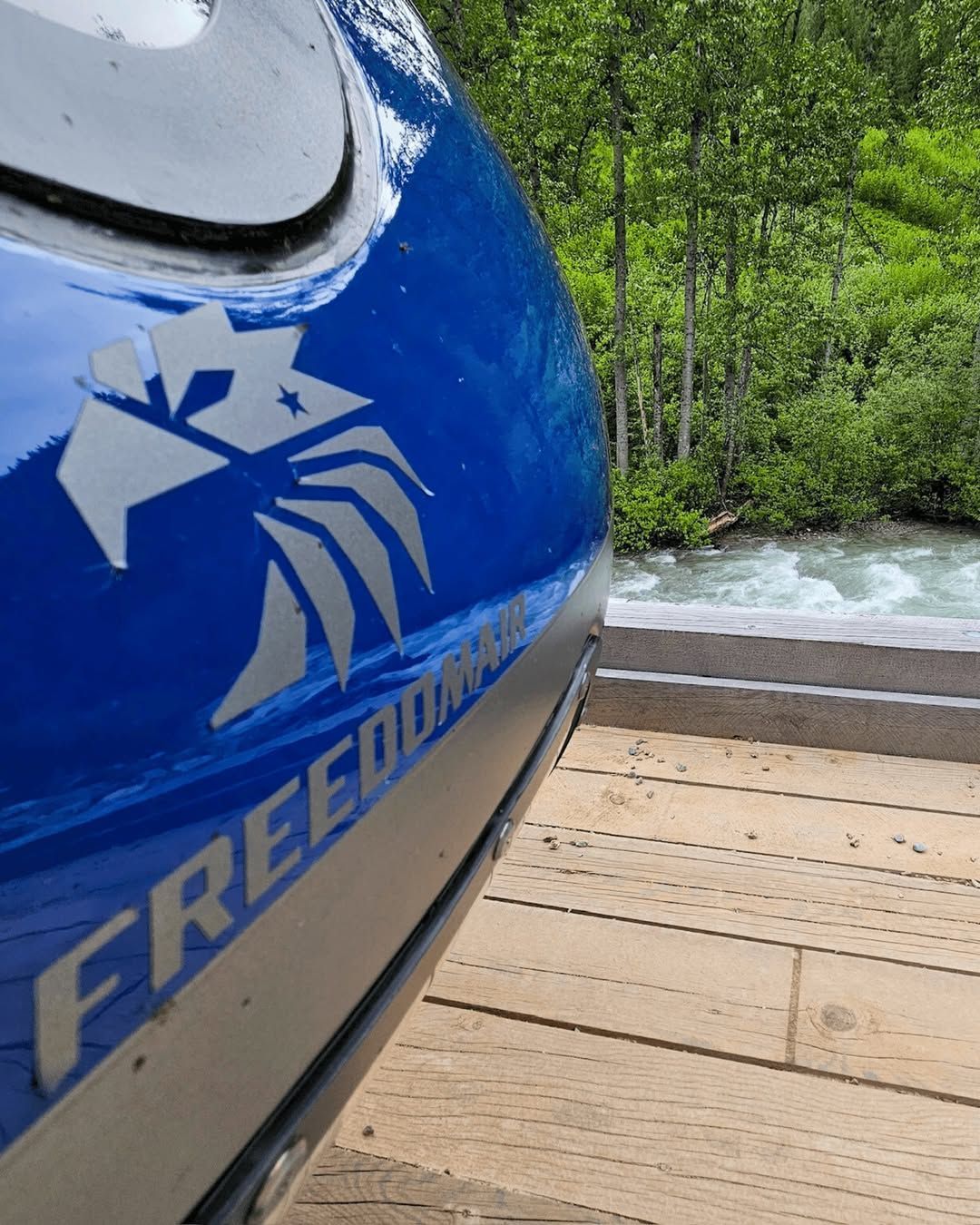 Blue kayak with eagle logo on wooden dock, river in the background.