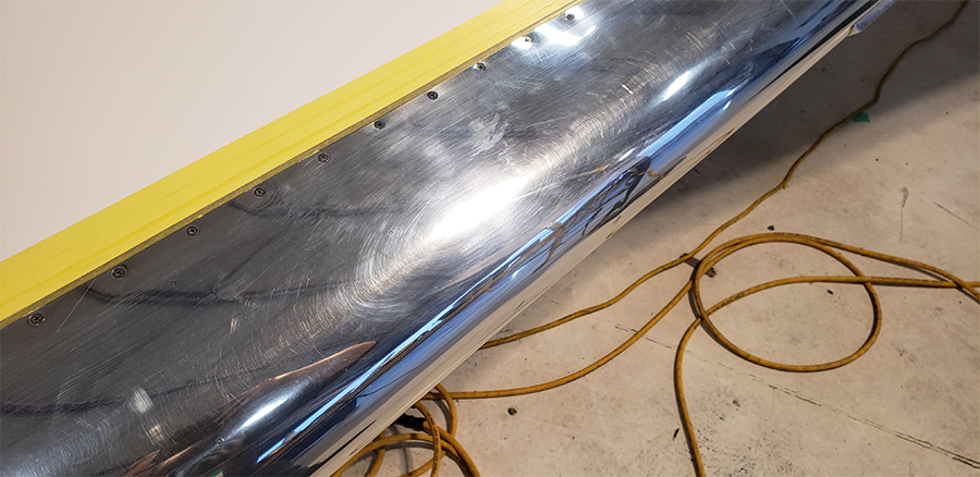 Shiny metal surface with yellow tape and an electrical cord on the floor.