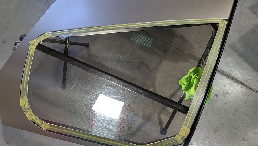 Car window with yellow tape around the edges, resting on a brown surface.