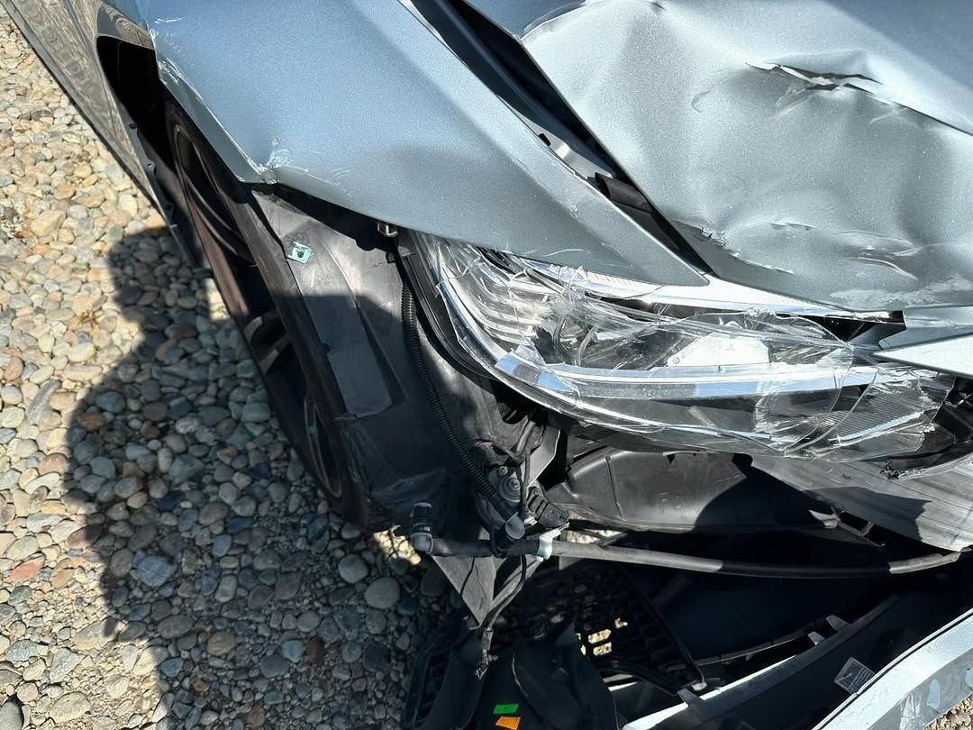 Damaged silver car front. Dent in bodywork above headlight, broken parts.