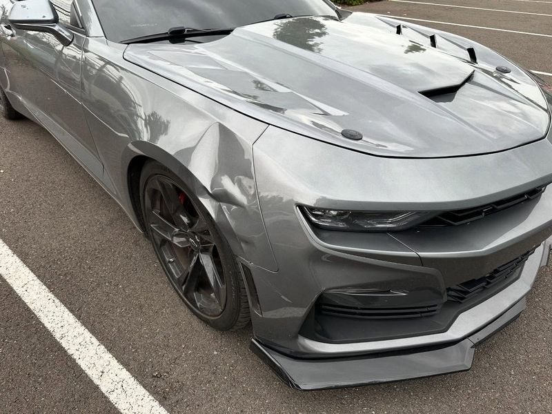 Gray Chevrolet Camaro with a custom hood and front splitter parked on asphalt.