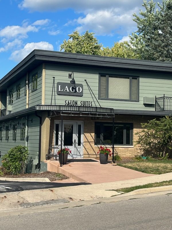 Lago Salon Suites building with green siding and black trim; light blue sky.