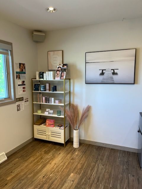 Corner of a room with skincare products on a gold shelf, a framed art print, and dried flower arrangement.