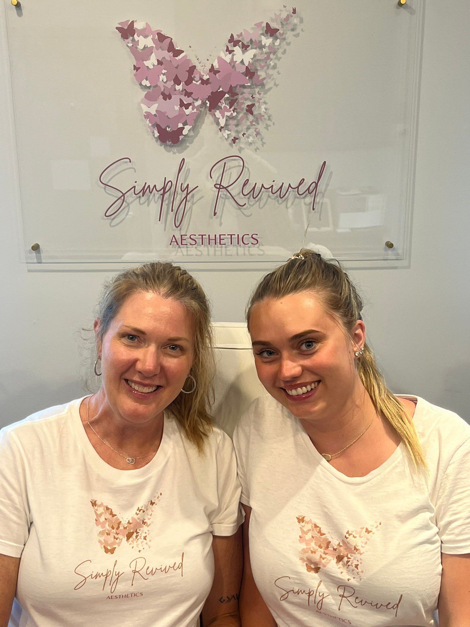 Two smiling women in white shirts with butterfly logo in front of a butterfly art piece.