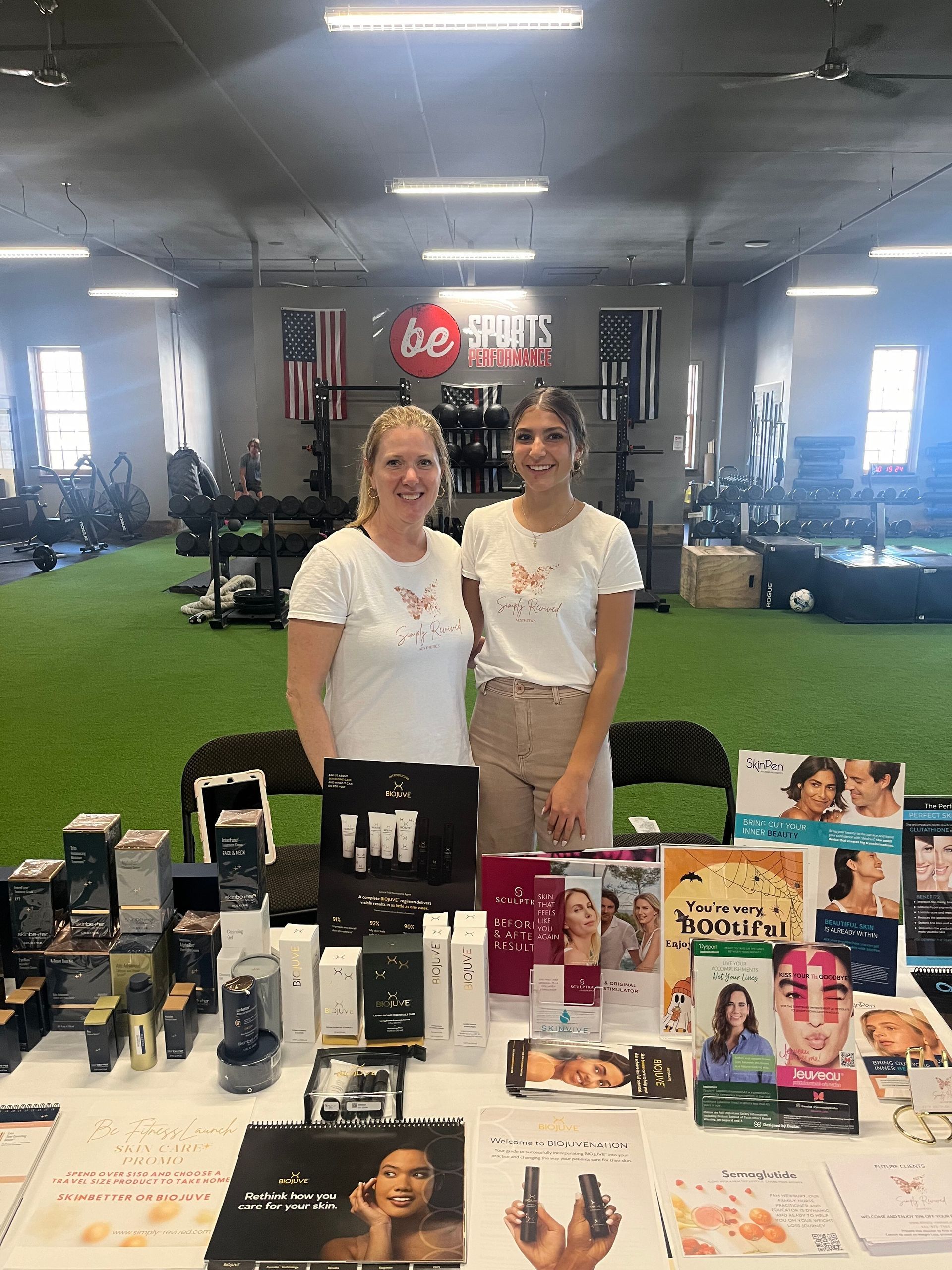 Two women stand behind a table of beauty products, promoting the brand at an event.