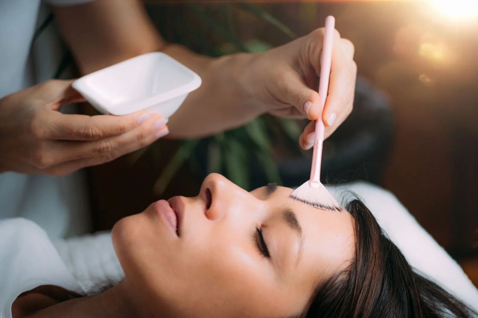 Spa therapist applying facial mask with brush to a reclining client