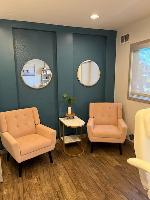 Two pink armchairs face a teal wall with round gold mirrors. A small table holds greenery.