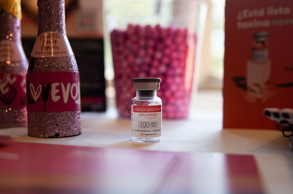 Vial of medication with pink label, bottle of pink glitter, and pink candies in the background.