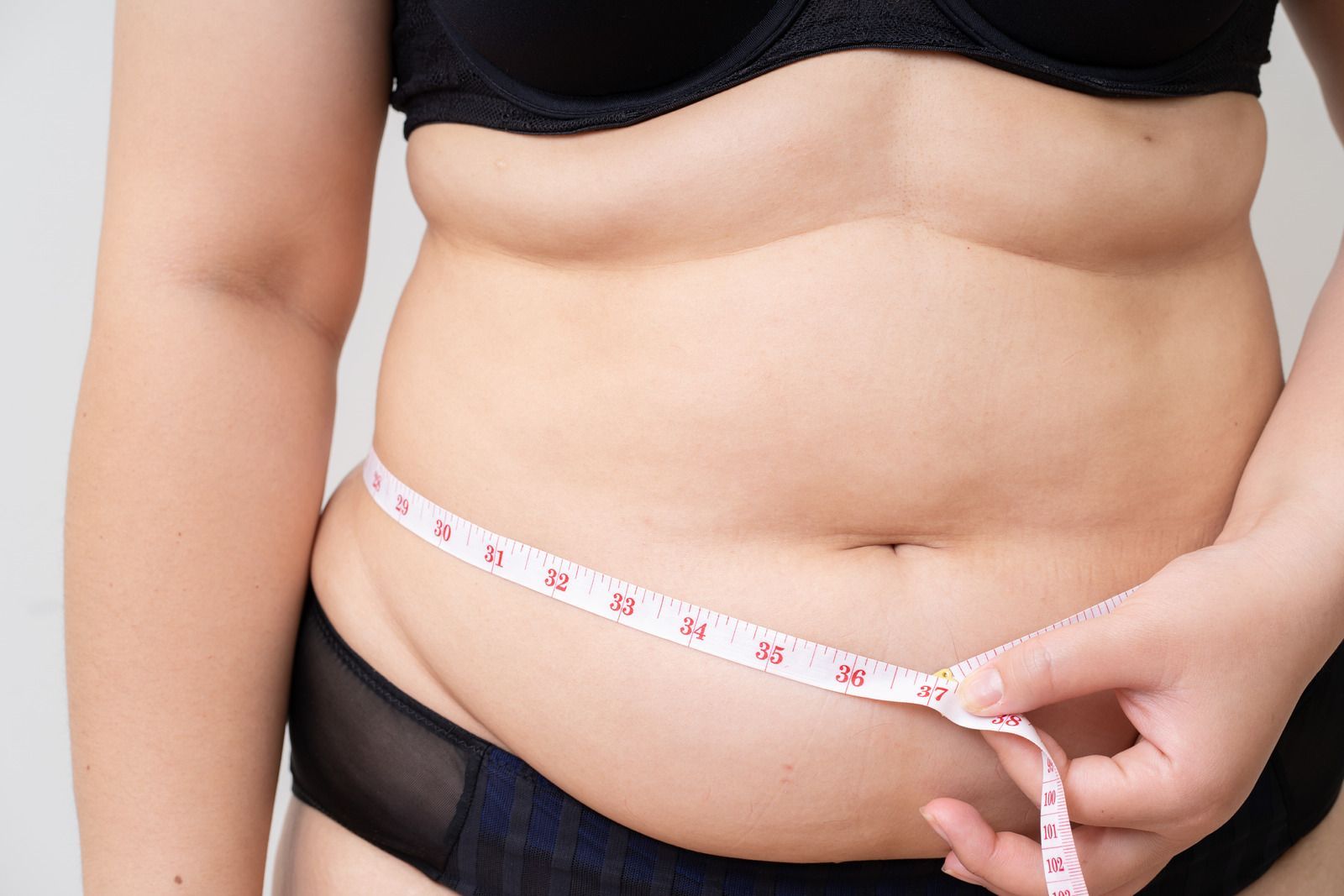 A woman is measuring her waist with a tape measure.