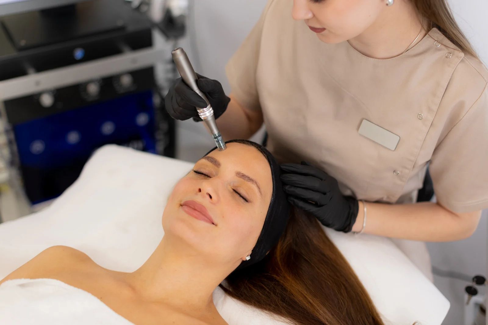 Woman receiving a microneedling treatment on her cheek, lying down in a spa setting. A
gloved hand