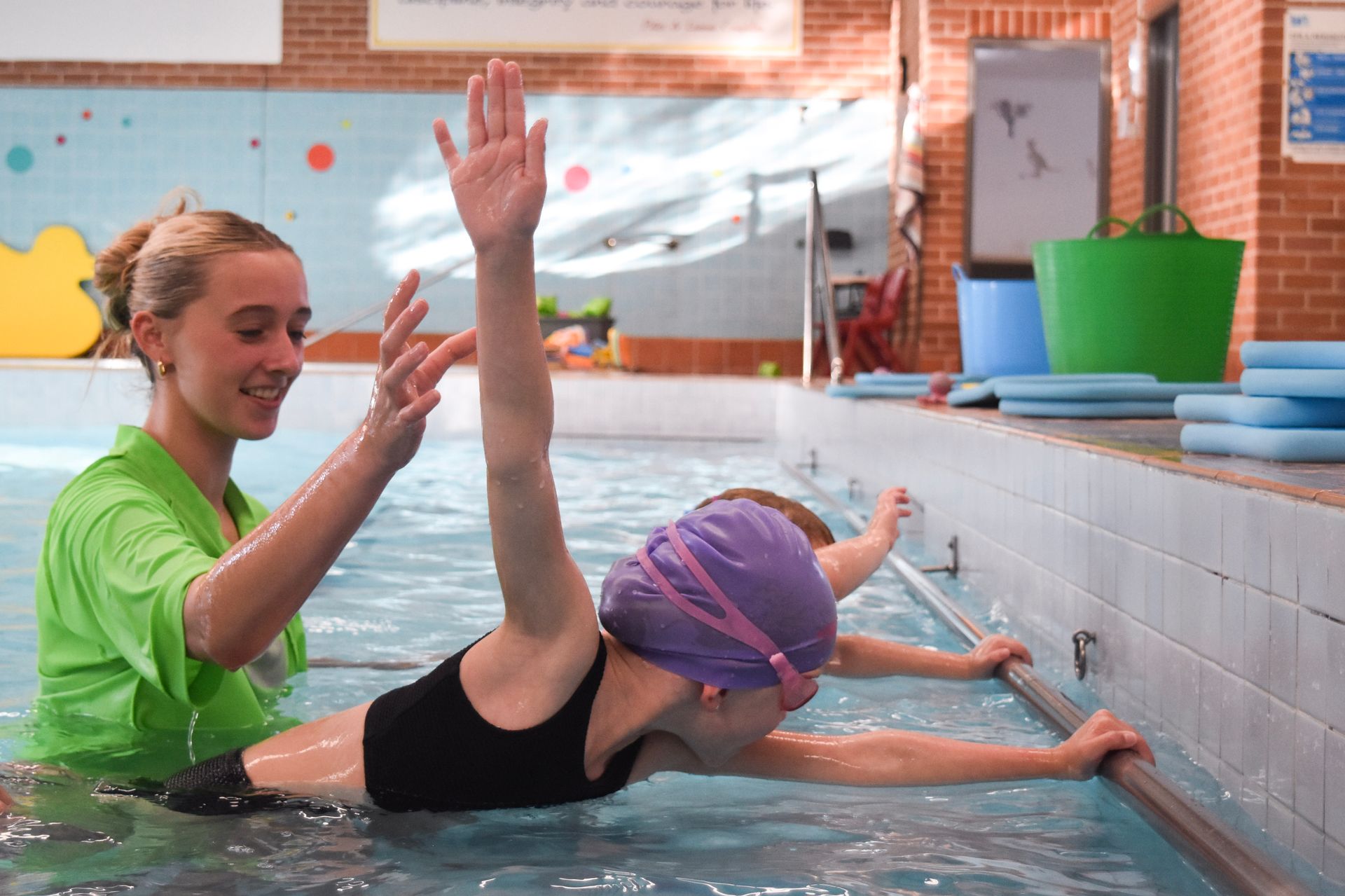A woman is teaching a young girl how to swim in a swimming pool.